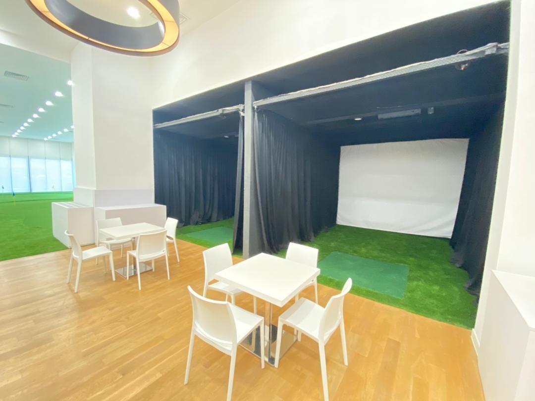 Indoor golf simulator bay with projection screen and artificial turf